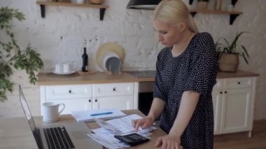 Genç bir kadın mutfakta duran faturaları öder. Ev bütçesini korur