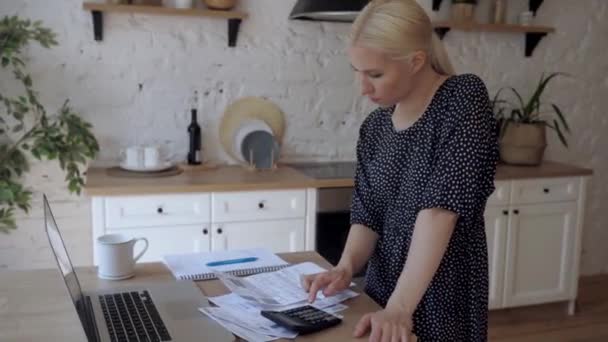 Een jonge vrouw betaalt voor bonnetjes die in de keuken staan. Houdt het huisbudget — Stockvideo