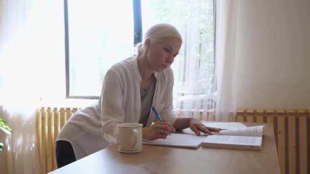 Meisje student studeren thuis aan de tafel.Maakt notities van een boek in een notebook — Stockvideo