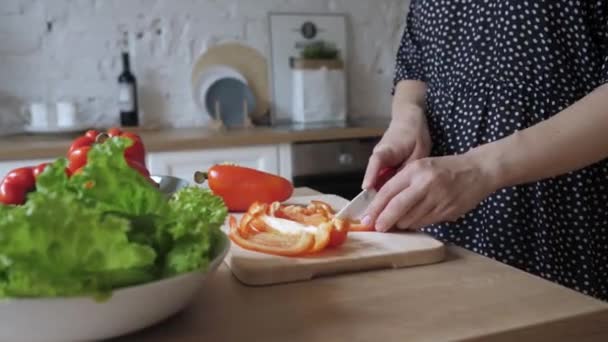 Hermosa joven ama de casa sostiene cuchillo cortes pimienta ensalada cocina plato de verduras. — Vídeo de stock