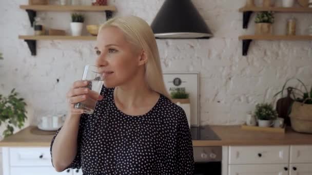 La chica bebe agua de un vaso de pie en la cocina luminosa. — Vídeos de Stock