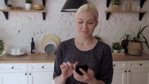 Femme debout dans la cuisine tenant téléphone intelligent profiter de chat distant avec des amis — Video