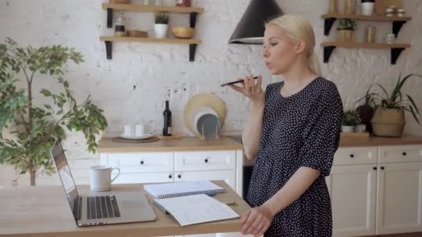 Schöne Hausfrau arbeitet in der Küche und nimmt Audiobotschaft am Telefon auf — Stockvideo