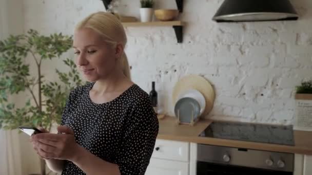 Жінка проводить час на кухні тримає телефон отримує довгоочікувані смс чудові новини — стокове відео