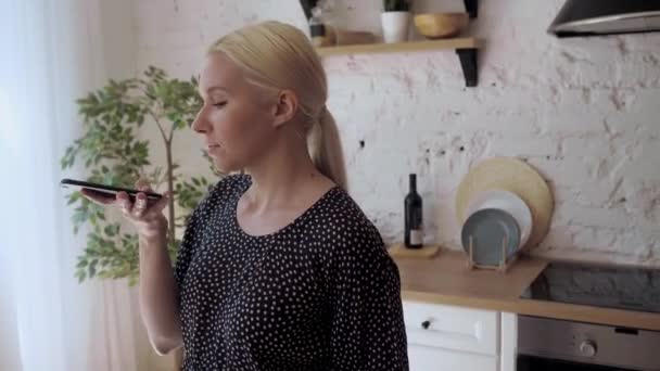 Woman standing in home kitchen having fun chatting with friend use speaker phone — Stock Video