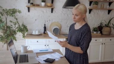Mutfakta duran genç bir kadın elektrik faturasını açıyor ve çok üzgün.
