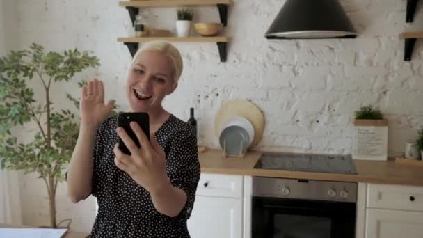 Jeune femme au foyer dans la cuisine parler avec un ami sur une vidéo à l'aide de votre smartphone — Video