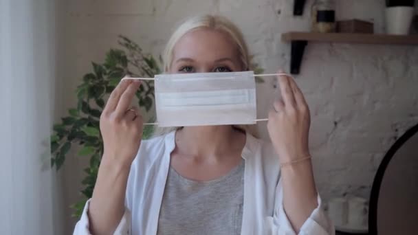 Молода мила блондинка одягає медичну маску . — стокове відео