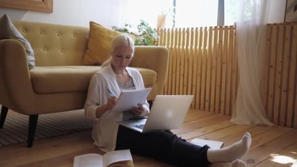 Jovem mulher bonita trabalha de casa no laptop e faz anotações em um notebook — Vídeo de Stock