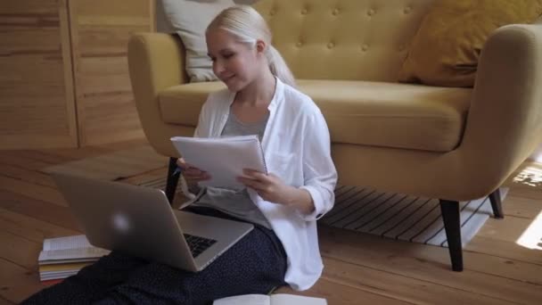 Junge hübsche Frau arbeitet von zu Hause aus am Laptop und macht sich Notizen in einem Notizbuch — Stockvideo