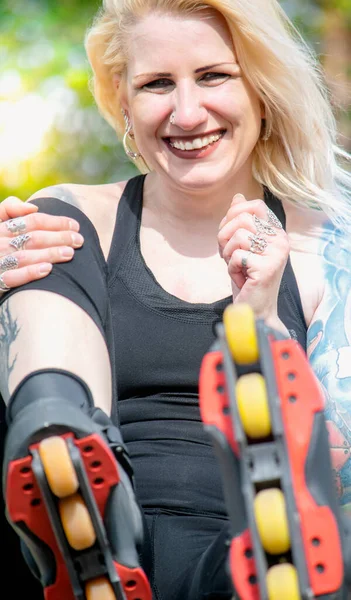 Glimlachende zittende blonde vrouw met rolschaatsen — Stockfoto
