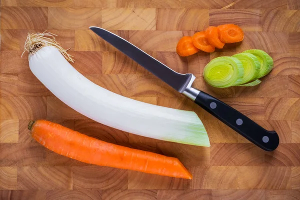 Wooden cutting board with knife, chopped leek and carrot