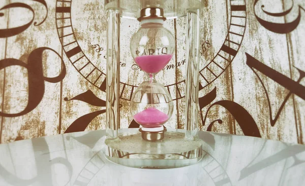 Tiny hourglass with pink sand on clock background