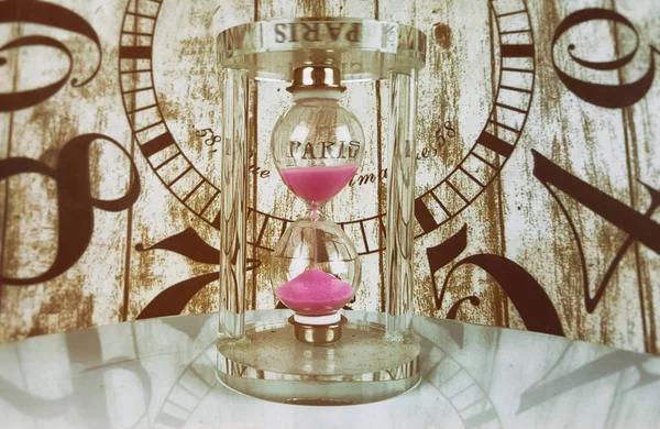 Hourglass with pink sand on clock background
