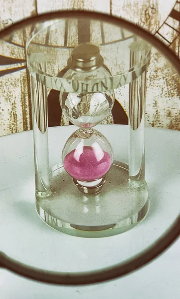 Tiny hourglass with pink sand on clock background