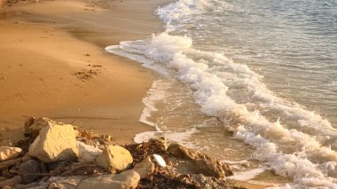 Dalgalar köpük ve açık kum ile kayalık deniz kıyısı