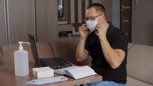 L'uomo indossa la maschera facciale, disinfetta le mani con antisettico prima di lavorare sul computer portatile — Video Stock