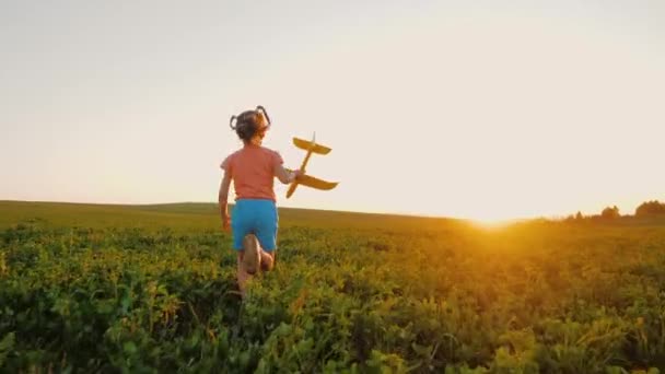 Zorgeloos klein meisje loopt met speelgoed vliegtuig op weide bij zonsondergang, speelgoed vliegtuig spelen — Stockvideo
