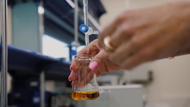 Próbka cieczy kapiącej do kolby laboratoryjnej i ręce naukowca wstrząsają nią. — Wideo stockowe