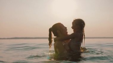 Neşeli anne gün batımında mutlu çocuğu suya daldırıyor, gülüyorlar ve gülüyorlar.