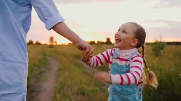 Mother and little daughter walks holding hands, skipping along road in field — Stock Video