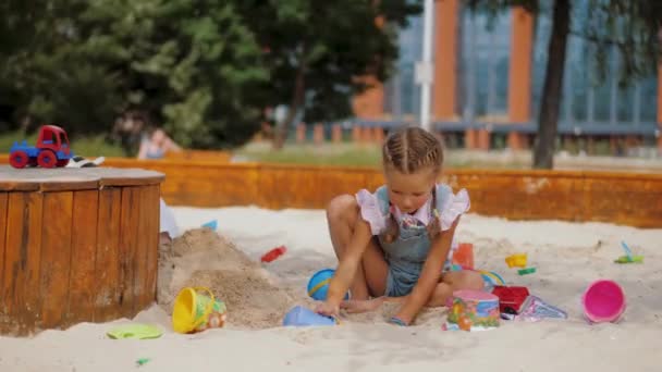 Meisje spelen met plastic speelgoed en emmers in zandbak in woonwijk — Stockvideo