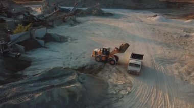 Taş ocağındaki ağır makineler, kazıcı taşları çöp kamyonuna yüklüyor.