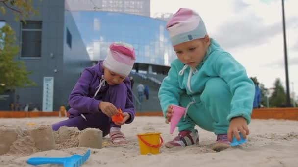 Two children 4-5 years old sitting in sandbox, playing with toys and buckets — Stock Video