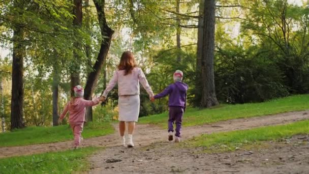 어머니는 자녀들과 함께 집 밖에 있는 공원에서 손을 잡고 걸어 다닌다. — 비디오