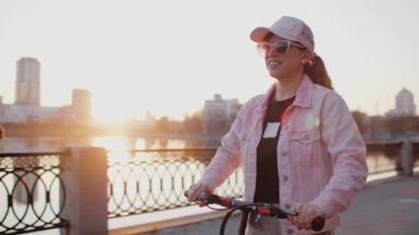 Elektrikli scooter kullanan çekici bir kadın gün batımında sette geziyor.