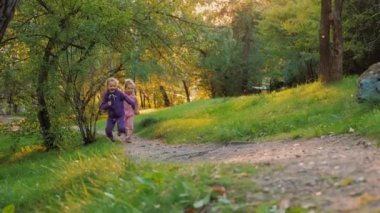 Mutlu çocuklar yaz parkında birlikte koşar, iki küçük kız kardeş arayı kapatır.