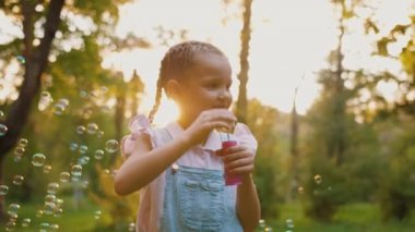 Güzel küçük kız sabun köpüğü üflüyor, mutlu şirin çocuk parkta oynuyor.