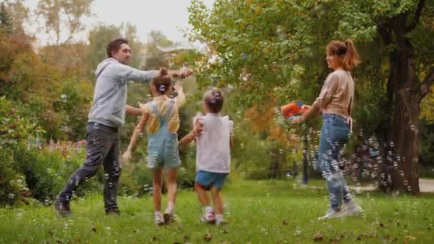 Los padres y los niños se divierten juntos con burbujas de jabón en el parque de verano — Vídeo de stock