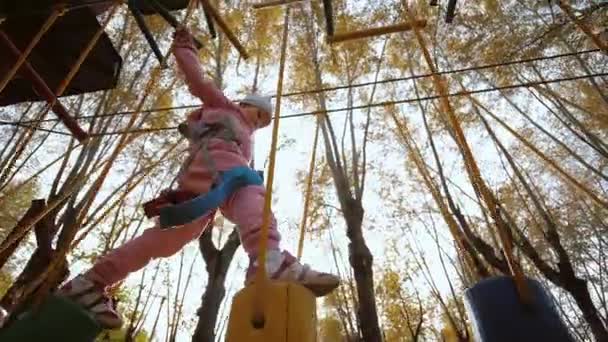 Menina caminhando e equilibrando em balançar toco de madeira no parque de corda — Vídeo de Stock