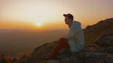 Hipster adam kayanın kenarında oturuyor, fincandan çay içiyor, günbatımının tadını çıkarıyor.