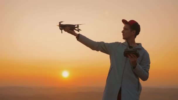Hombre comienza dron de su mano, avión despega contra el telón de fondo de la puesta del sol — Vídeos de Stock