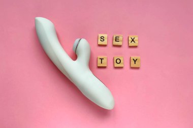 Seks oyuncağı. Pembe arka planda beyaz klitoral vibratör. Yazılı seks oyuncağı. Yetişkinler için kullanışlı, seks dükkanı