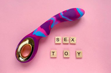 Seks oyuncağı. Pembe arka planda renkli seks vibratörü. Yazılı seks oyuncağı. Yetişkinler için kullanışlı, seks dükkanı