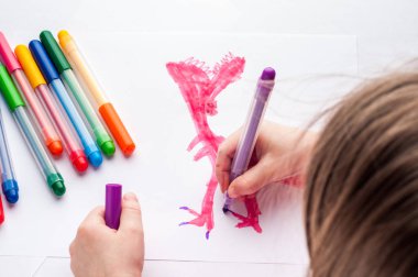 beyaz bir kağıda işaretçilerle çocuk çizer