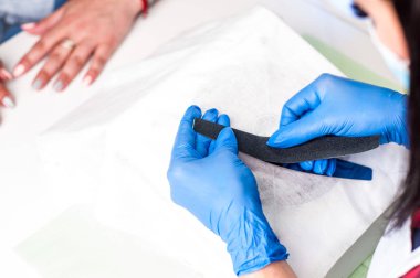 Bir kadın müşteri elleri üzerinde Manikürcü iş, onu çivi güzel görünmesi. Salon prosedürü devam ediyor. Sterilite için eldivenlerde profesyonel çalışmalar