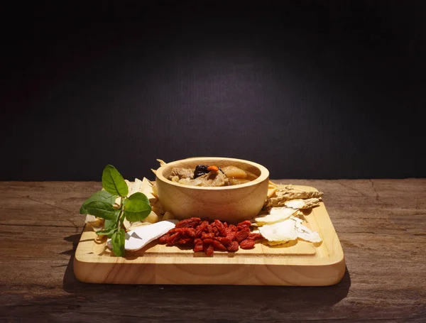 Bowl of chinese soup and herbal medicines on wood against black
