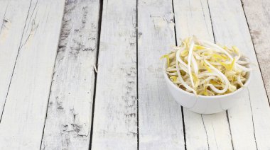 Beyaz ahşap arka planda bir kase taze fasulye filizi.