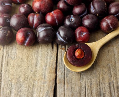 Bir grup erik, ahşap masanın üstüne ve bir buçuk kaşık da kaşığın üzerine serilmişti.