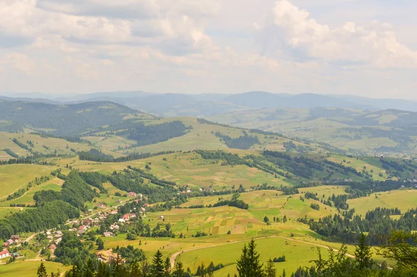 Yükseklikten muhteşem bir manzara. Gökyüzüne karşı dağlardaki yeşil orman ve köy. Ukrayna Karpatları.