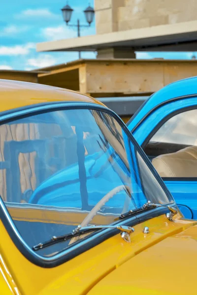 Car hood and windshield of a yellow car on the background of a blue car close-up