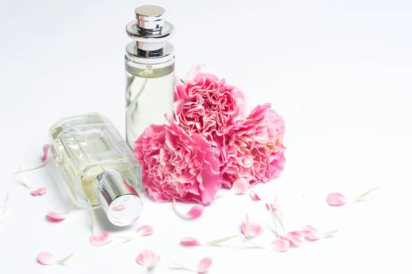 Parfémy a růžové karafiáty na bílém pozadí — Stock fotografie