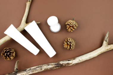 Ahşap dallarda beyaz sıkışan borular, kahverengi arka planda duran krema şişeleri. Güzel cilt bakımı. Organik, biyolojik ve doğal kozmetik konsepti. Güzellik ve kaplıca konsepti. Stok fotoğrafı