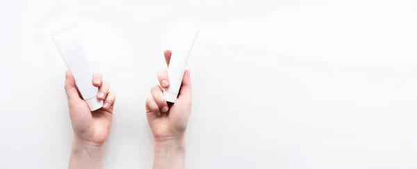 Mãos femininas com frasco de espremer recipientes de tubo de plástico de creme isolado no fundo branco vista superior cópia espaço flat lay. Cuidados com a pele da beleza, conceito cosmético natural. Modelo de banner web. Foto stock — Fotografia de Stock