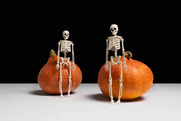 Esqueletos y calabazas naranjas sobre mesa blanca, fondo negro vista lateral espacio de copia. Fiesta de Halloween. Decoraciones espeluznantes. Fiesta nocturna. Composición creativa de horror. Foto de stock. —  Fotos de Stock