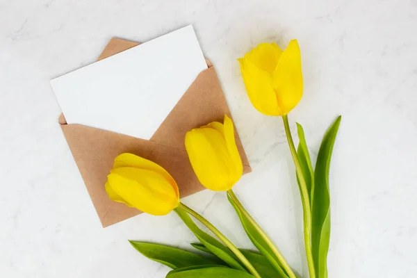 Boeket van gele tulpen, enveloppe en brief plat lag op marmeren achtergrond bovenaanzicht met kopieerruimte. Voorjaarsbloemen. — Stockfoto